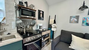 A modern kitchen with a stove, microwave, and toaster, a grey sofa, and artwork on the walls. - Italian Cottage Travel Nurses, Corporate Professionals - Dallas Medical District (Dallas)