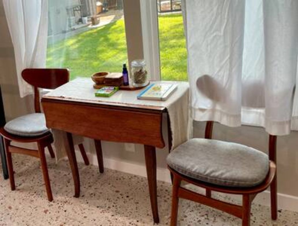 A dining area with a table and two chairs, a window with curtains, and a view of a green lawn.
