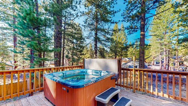Ein Whirlpool auf einer Holzterrasse mit Holzgeländer, umgeben von hohen Bäumen.