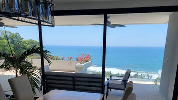 Un comedor con mesa y sillas de madera, una lámpara colgante y vista al océano.