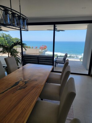 Ein Essbereich mit Holztisch und -stühlen, einer Hängelampe und Blick auf den Ozean.