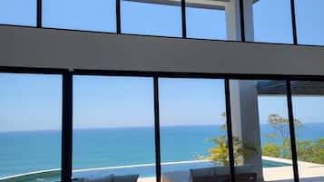 Un interior moderno con amplios ventanales que dan a una playa y al océano.