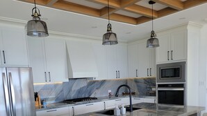 Een moderne keuken met witte kasten, een marmeren aanrechtblad, roestvrijstalen apparatuur en hangende verlichting.