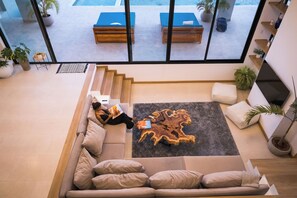 A modern living room with a sofa, coffee table, and a view of a pool area. - Mountain Top Mansion with Amazing Ocean Views - Brand New (Playa Hermosa)