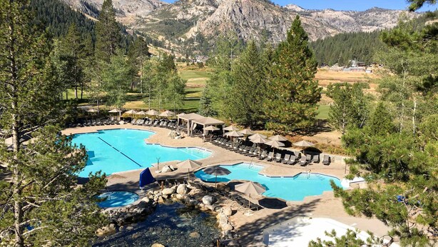 A resort with multiple swimming pools, lounge areas, and a mountainous backdrop. - Everline Resort & Spa Ski-in-ski-out condo with elevator, pool, hot tub, & spa (Olympic Valley)