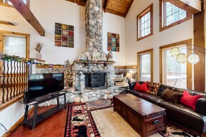 A cozy living room with a stone fireplace, a leather sofa, and a television. - Family friendly cabin with a private hot tub & access to a shared pool, tennis (Truckee)