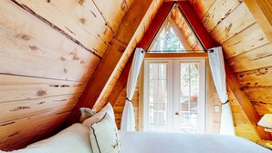 Een houten kamer met een bed, witte gordijnen en een raam.
