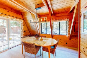 A wooden interior with a round table, wicker chairs, and a hanging light fixture. - Dog-friendly A-frame cabin with 2 decks & fireplace - walk to the beach (Homewood)