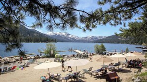 A lakeside beach with lounge chairs, umbrellas, and a view of snow-capped mountains. - Dog-friendly lakefront home with fast WiFi, private dock, & 180-degree views (Truckee)