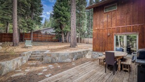 A wooden deck with stone steps, a dining table with chairs, and a barbecue grill. - Grand lodge in the woods near golf, hiking & skiing with multiple fireplaces (South Lake Tahoe)