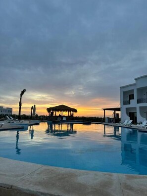 A swimming pool with lounge chairs, a covered seating area, and a modern building. - Marvista Resort Dahab (Dahab)
