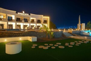 A modern hotel with a pool area, outdoor seating, and a view of the city skyline.
