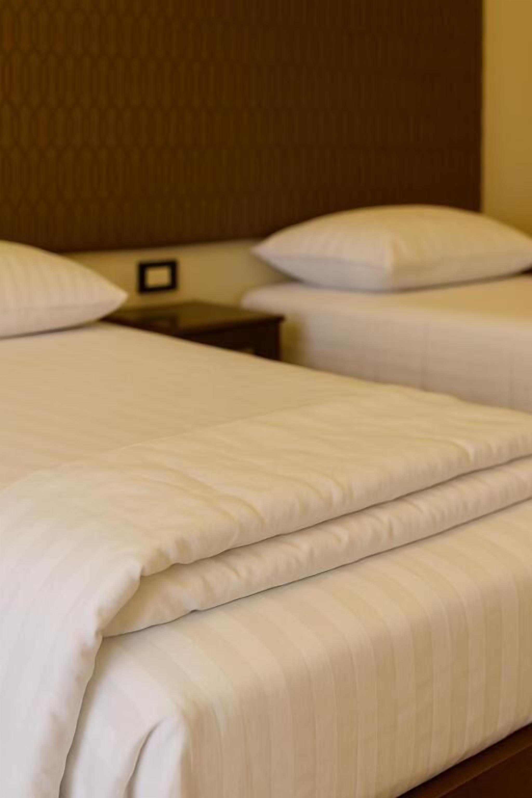 Una habitación de hotel con una cama bien tendida, un cabecero de madera y una mesita de noche con una lámpara.