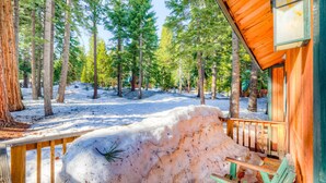Una cabaña de madera con un porche, rodeada de nieve y altos pinos.