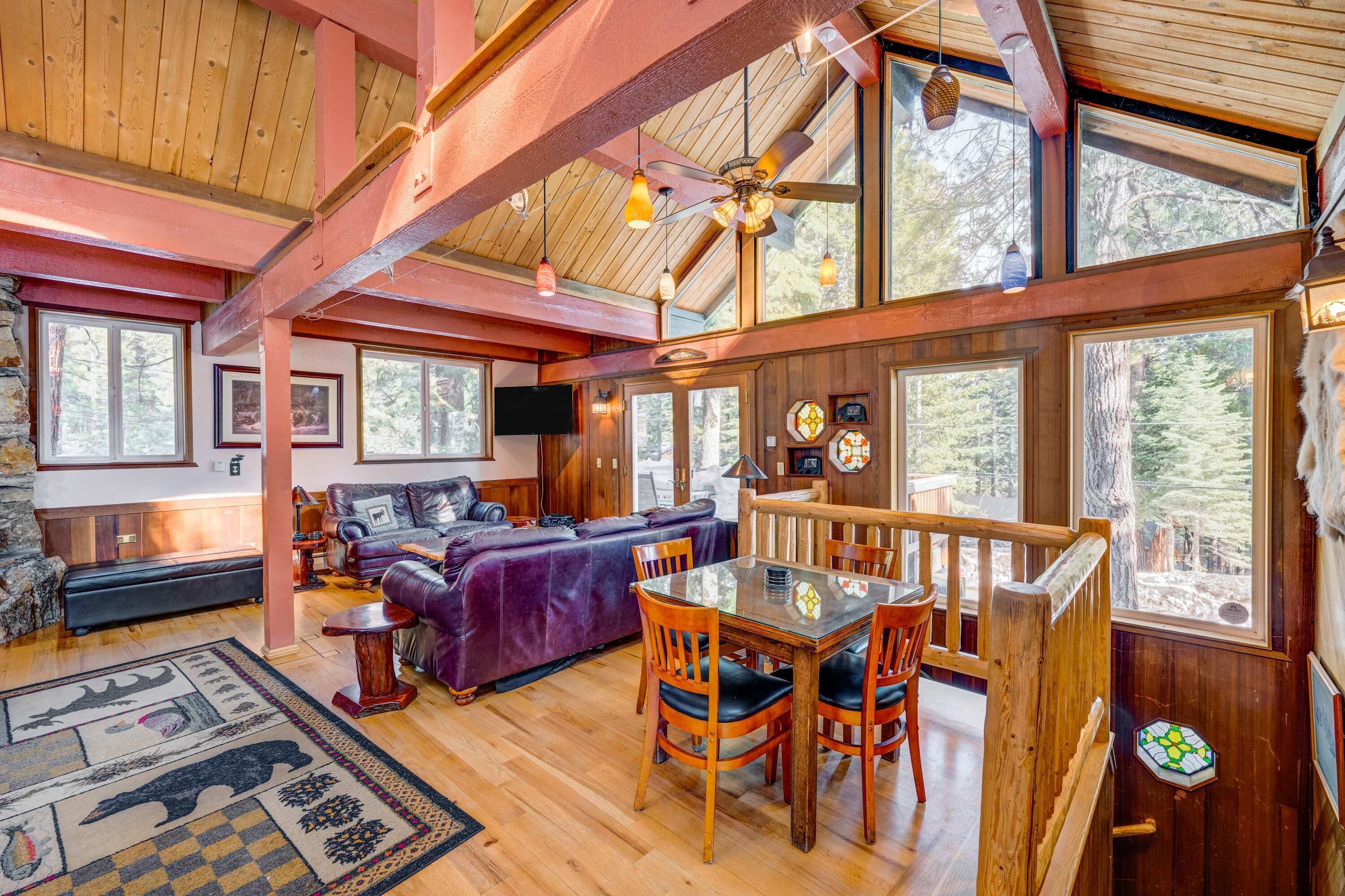 A cozy cabin interior with a dining area, wooden furniture, and large windows offering views of the forest.