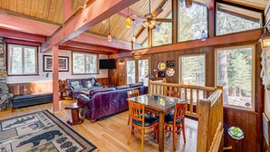 Interior acogedor de una cabaña con comedor, muebles de madera y grandes ventanales que dan al bosque.