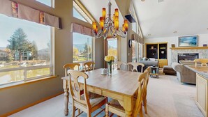 A spacious dining area with a large wooden table and chairs, a chandelier, and large windows offering a view of the outdoors. - Charming Tahoe Keys Waterfront Retreat with Private Dock, Pool Table (South Lake Tahoe)