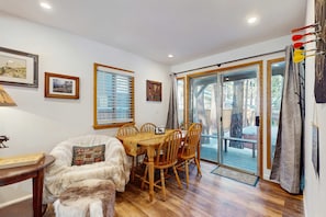A cozy room with a wooden dining table, chairs, a sofa, and a window with blinds. - Family-Friendly Cabin with Spa, Two Decks, Fenced Yard and Play Structure (South Lake Tahoe)