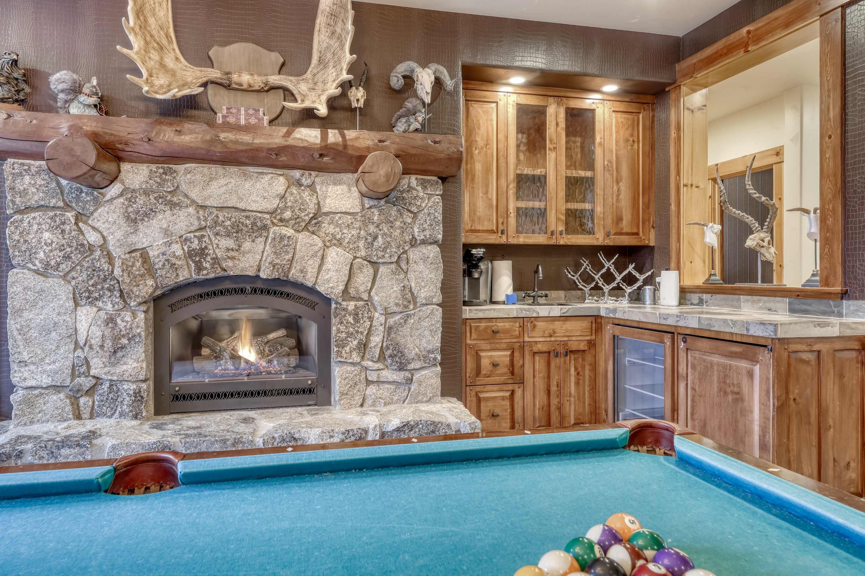 Une cheminée en pierre avec un feu de bois, des meubles en bois, une table de billard et un grand miroir.