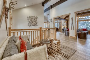 A spacious living area with a wooden railing, a sofa with cushions, a small round table, and a stack of logs.