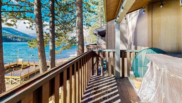 Um deck de madeira com vista para um lago e montanhas, uma área de estar coberta e um ventilador.