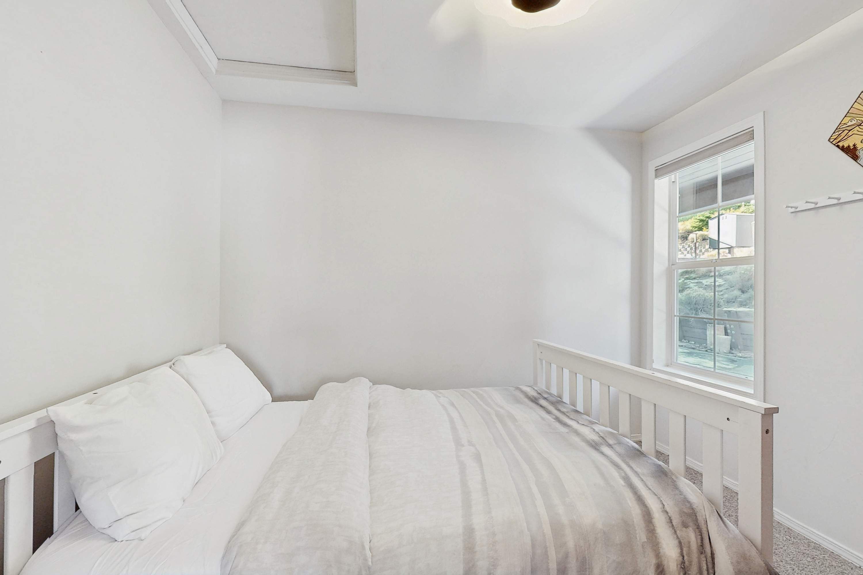 Ein Schlafzimmer mit Bett, weißen Wänden, einem Fenster und einer Deckenleuchte.