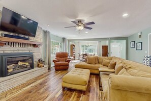 Ein Wohnzimmer mit Kamin, Fernseher, Deckenventilator und einem Ecksofa.