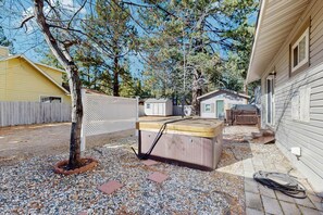 Un jardin avec un jacuzzi, une terrasse en bois et une zone délimitée par une clôture.