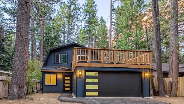 Una casa a due piani con un garage, circondata da alberi alti.