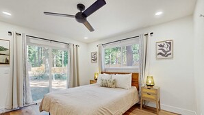 Una camera da letto con un letto, una ventola a soffitto, un comodino con una lampada e una finestra con tende.