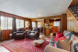 A spacious living room with leather chairs, a glass coffee table, a patterned rug, and a sofa with pillows. A kitchen is visible in the background. - Classic Gambrel-style cabin, family and pet friendly, walk to lake, close to ski (South Lake Tahoe)