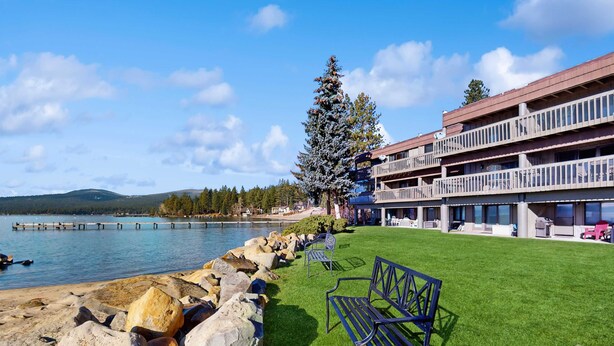 Ein Hotel am Seeufer mit einer Rasenfläche, einer Bank und Blick auf das Wasser.