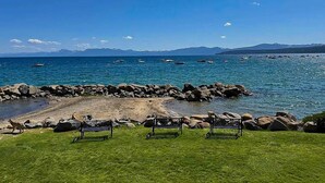 Eine Küstenansicht mit felsiger Küste, einer grasbewachsenen Fläche mit Bänken und Booten auf dem Wasser.