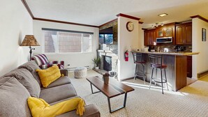 Ein Wohnzimmer mit einer Couch, einem Couchtisch und einer Küchenzeile inklusive Bar und Barhocker.