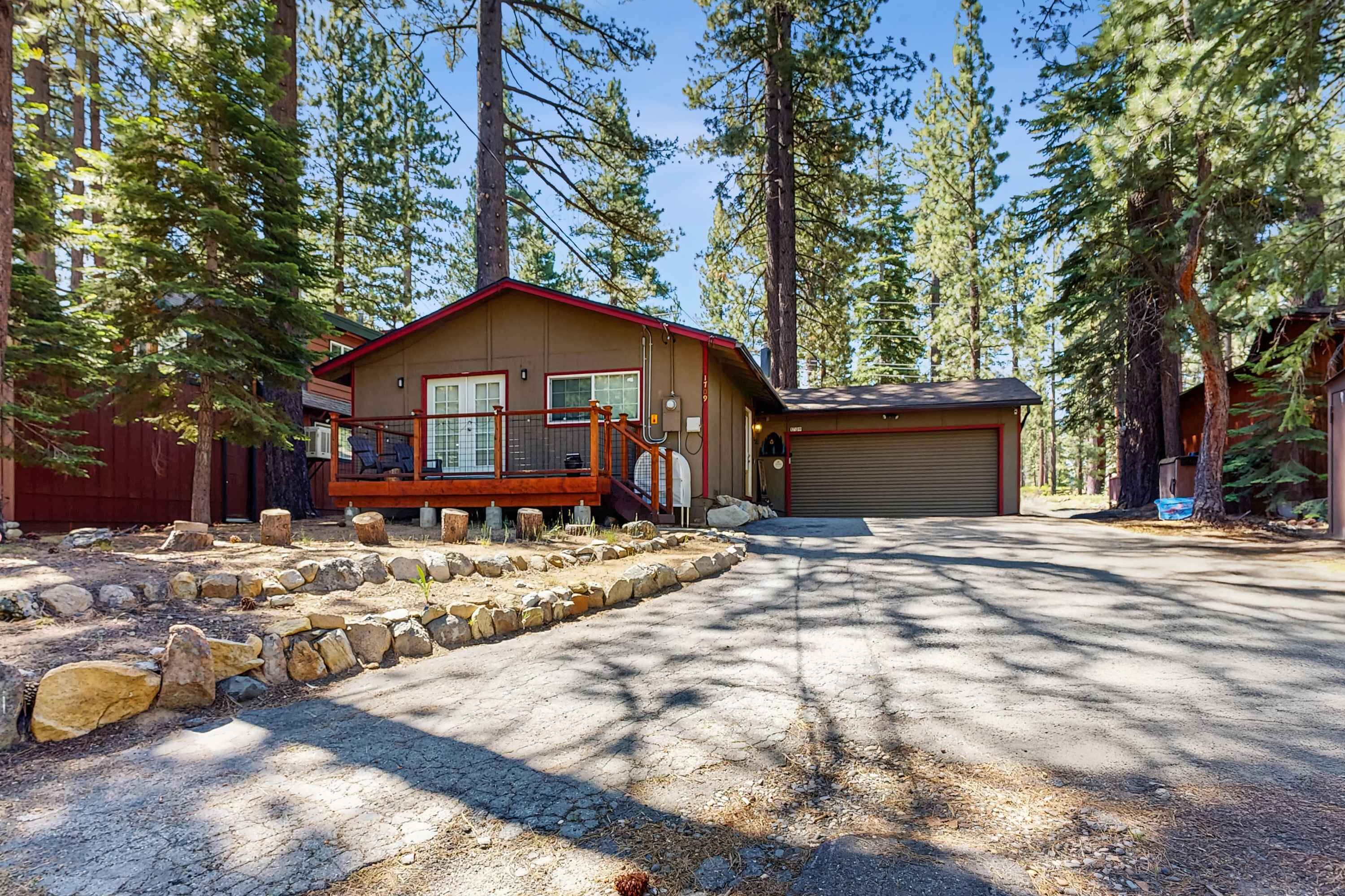 A cabin with a wooden deck, a garage, and a stone pathway.