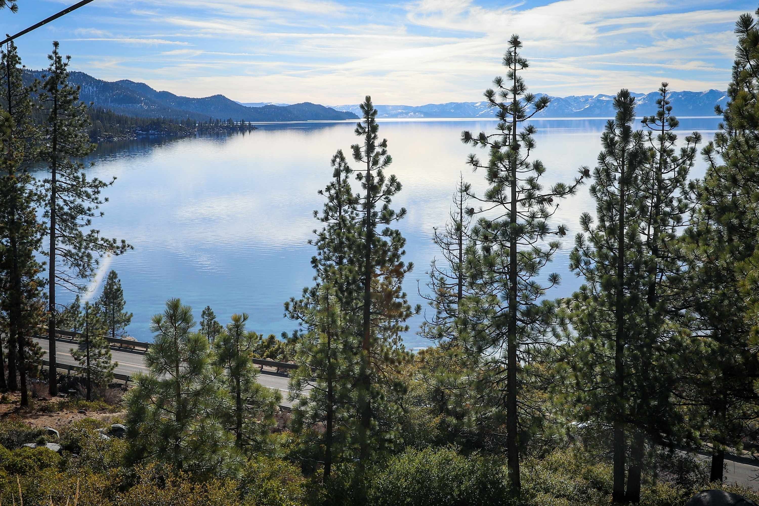 Un lac bordé de montagnes au loin, entouré d’arbres.