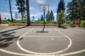 Un terrain de basket en plein air, avec un panier, entouré d’arbres et agrémenté d’un banc.