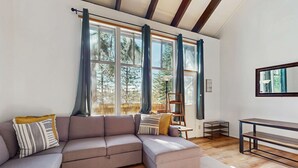 A modern living room with a sectional sofa, a wooden floor, and large windows with curtains. - Cozy and Convenient Condo with Fireplace, Deck, W&D, Close to Town, Lake, Trails (Tahoe City)