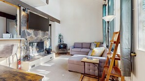 A living room with a fireplace, sofa, and a wooden ladder. - Cozy and Convenient Condo with Fireplace, Deck, W&D, Close to Town, Lake, Trails (Tahoe City)