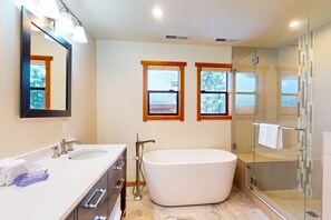 Un baño moderno con una bañera independiente, dos lavamanos, un espejo grande y una ducha con mampara de cristal.