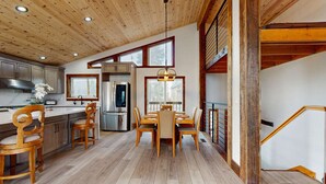 A modern kitchen with wooden flooring, a dining area with a wooden table and chairs, and a staircase with a wooden railing. - Pristine Family and Dog Friendly Mountain Home with Deck, BBQ, W&D (Truckee)