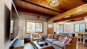 Una sala de estar acogedora con techo de madera, un sofá con almohadas que dicen 'LOVE', una mesa de centro y un comedor con mesa y sillas.