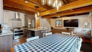 Una cocina moderna con electrodomésticos de acero inoxidable, un comedor con mantel a cuadros y una sala de estar acogedora con televisor y asientos.