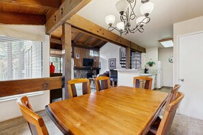 A dining area with a wooden table and chairs, a chandelier, and a kitchen in the background. - Beautiful Condo with private beach access, shared pools & hot tubs (South Lake Tahoe)