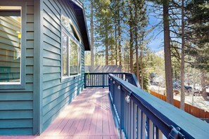 Eine Holzterrasse mit blauer Geländer, umgeben von Bäumen und einem Berg im Hintergrund.