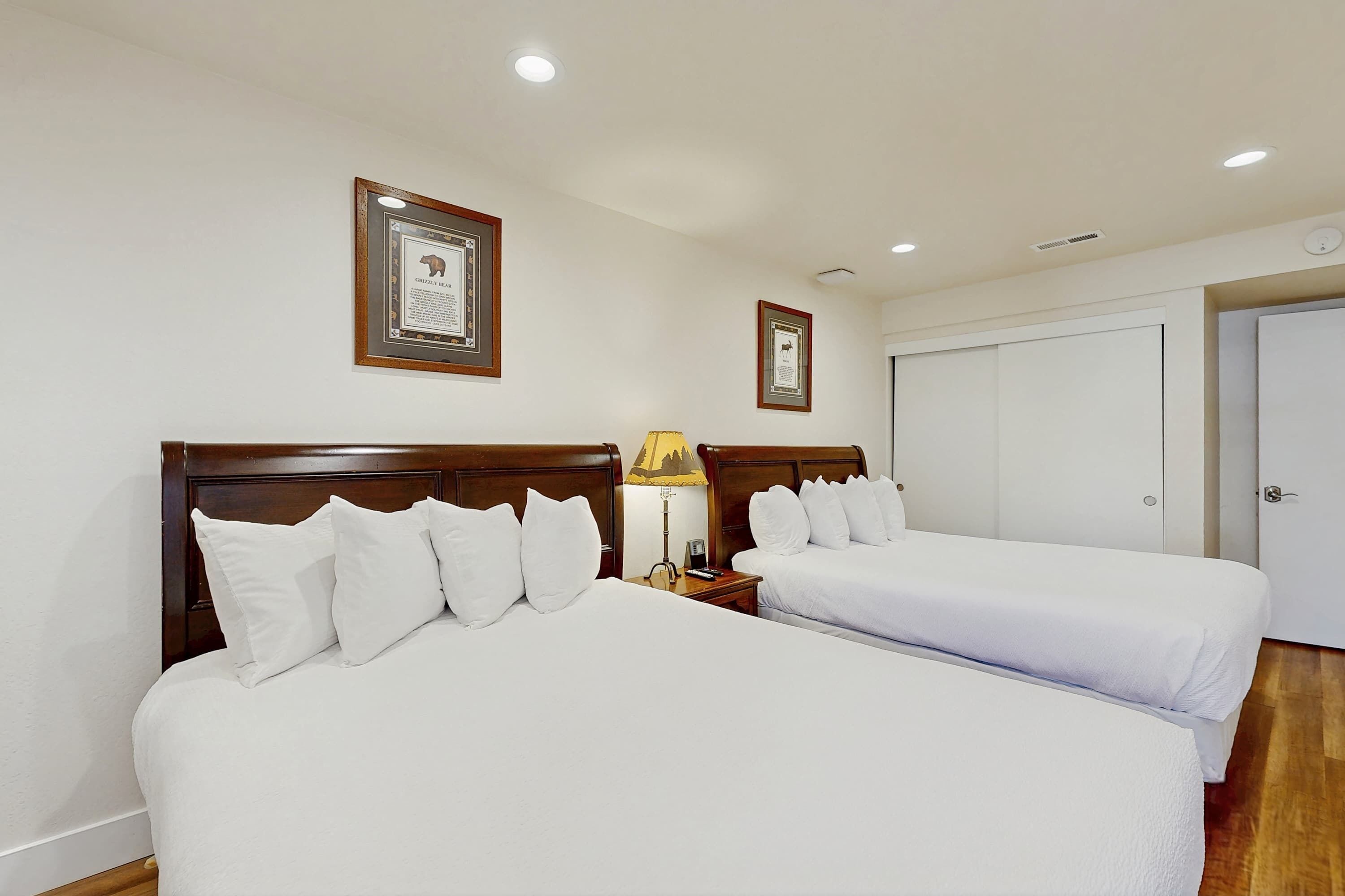 Een hotelkamer met twee bedden, een houten hoofdbord, een nachtkastje met een lamp en ingekaderde certificaten aan de muur.