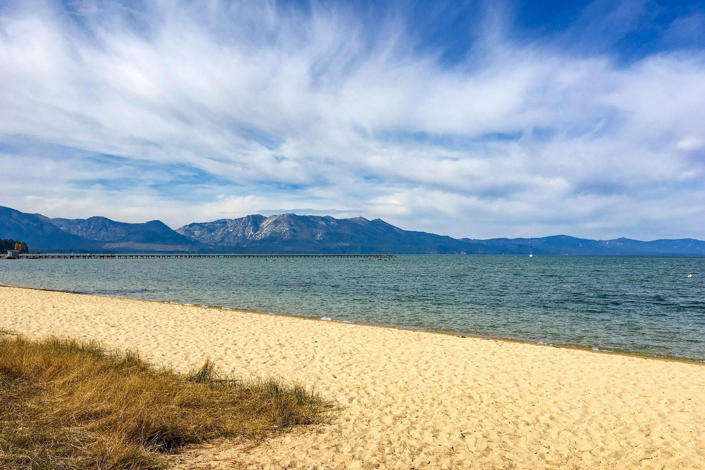 A beach with a clear view of mountains in the background and a pier extending into the water.