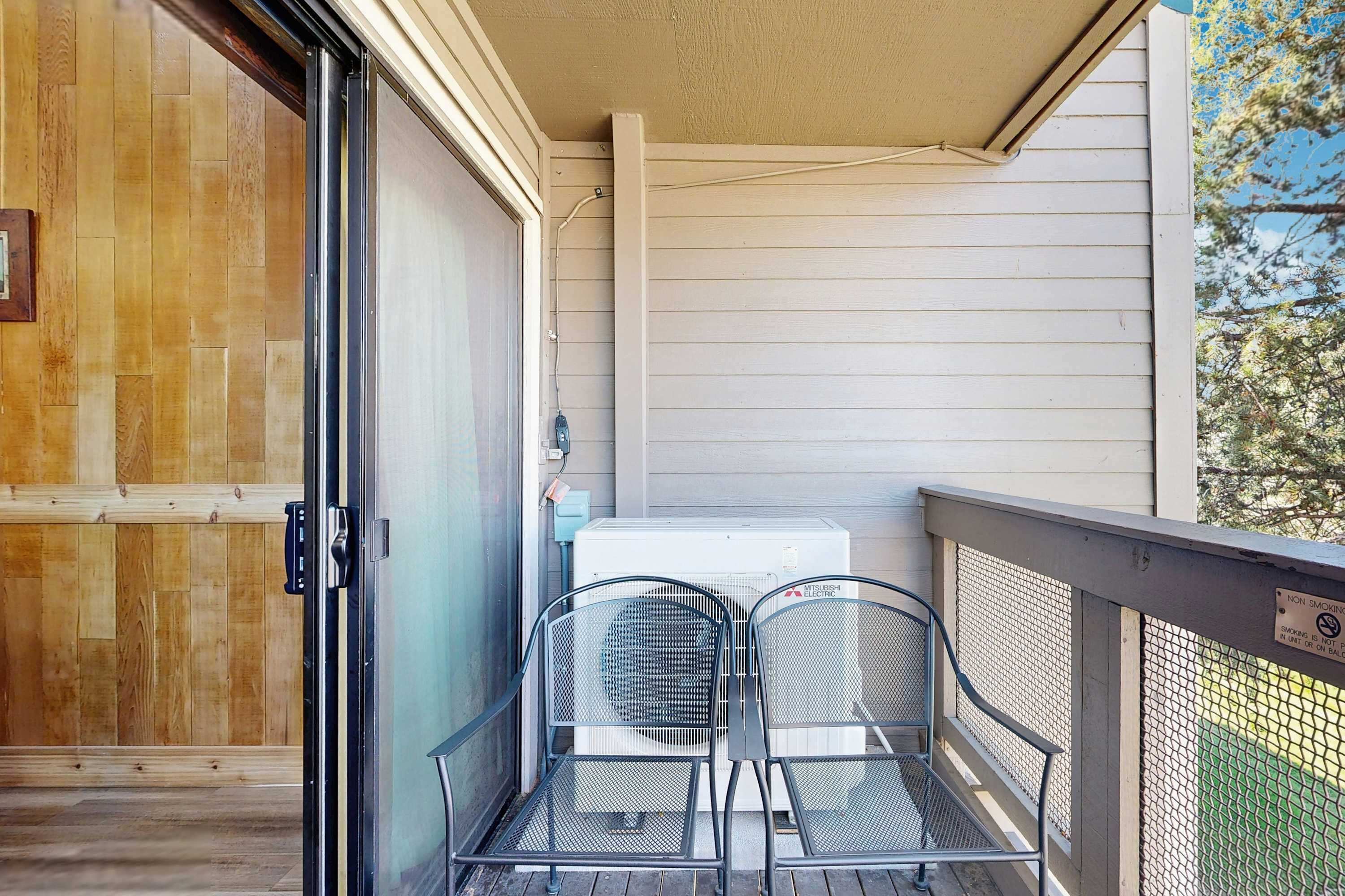 Een balkon met twee metalen stoelen, een schuifglazen deur en een airconditioning.