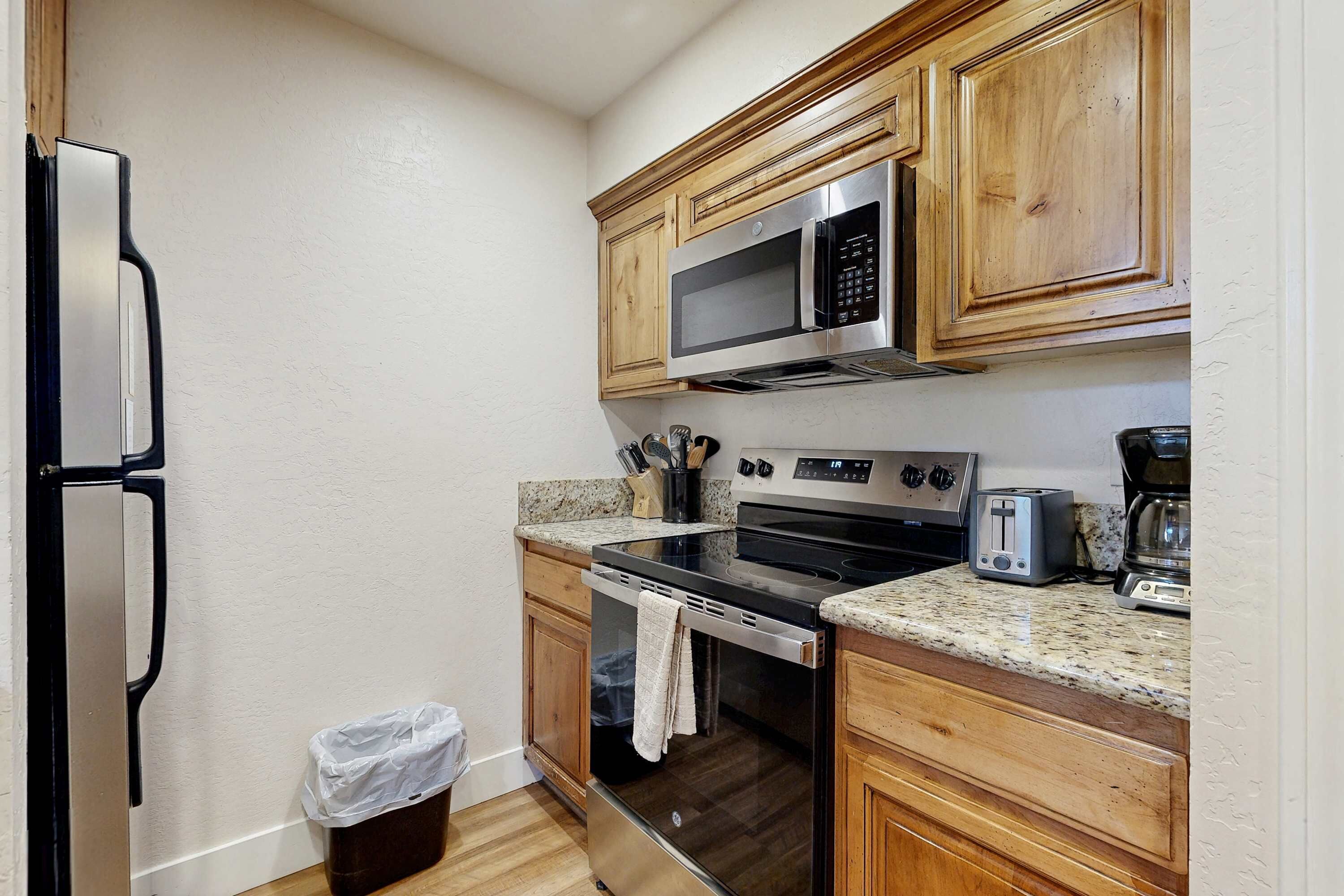 A kitchen with wooden cabinets, a stainless steel refrigerator, a microwave, an oven, a toaster, and a coffee maker.