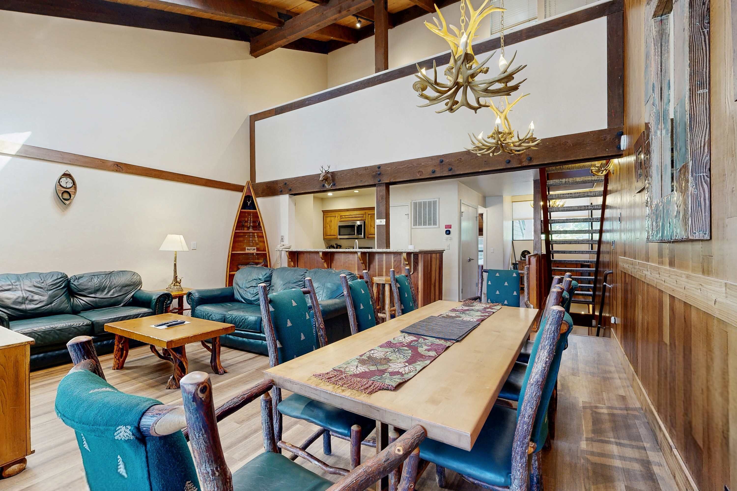 Un interior rústico con una mesa de comedor de madera, sillas tapizadas en azul, un sofá de cuero y una araña.